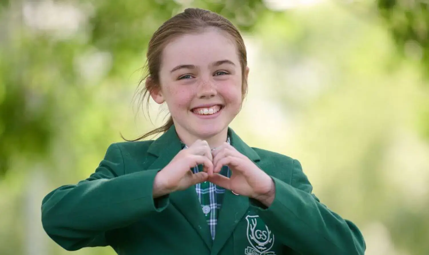 The Grange Junior School pupil making a heart shape with their hands and smiling.
