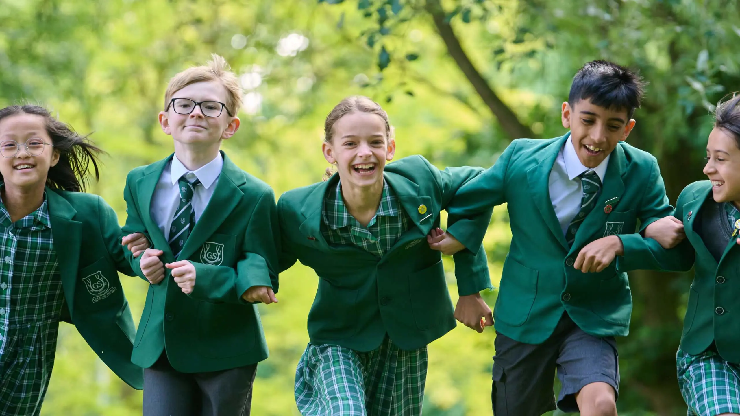 Children running through woodland arm in arm.